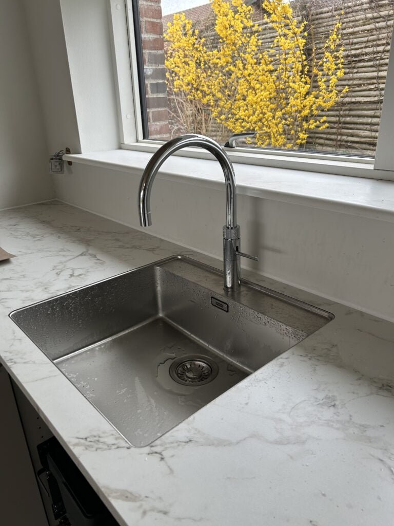 Moderne køkkenvask med marmorbordplade ved vindue