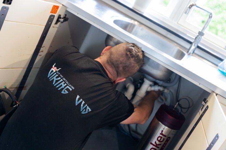 VVS-installatør reparerer rør under køkkenvask